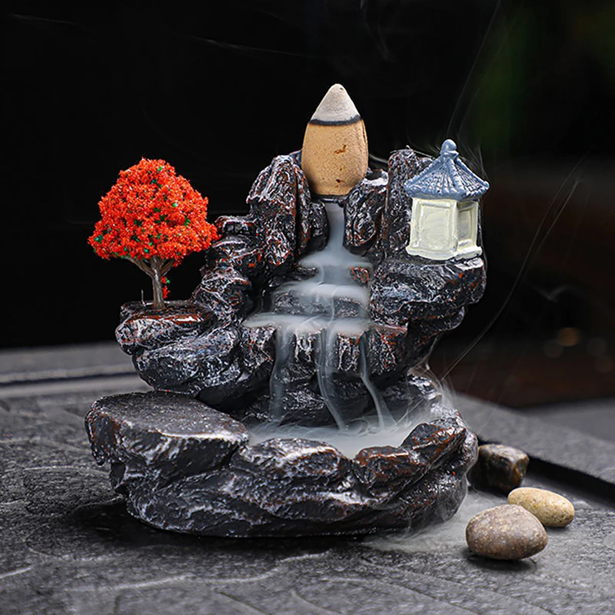 Decorative water fountain with rocks, tree, and lantern on a dark background